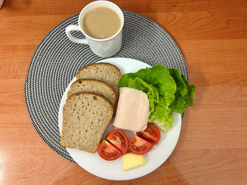 Na zdjęciu: Kawa z mlekiem, Chleb Graham, Masło extra 82%, Blok drobiowy - wędlina drobiowa parzona, Pomidor, Sałata zielona